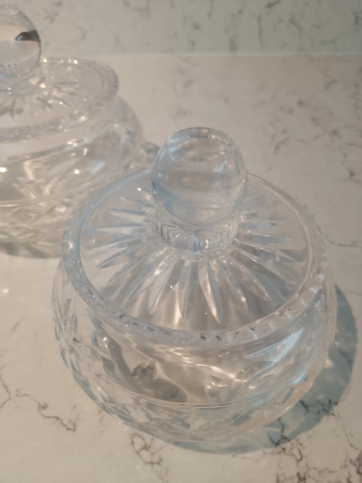 Vintage Stuart crystal jars with intricate cut designs and clear glass lids on marble surface