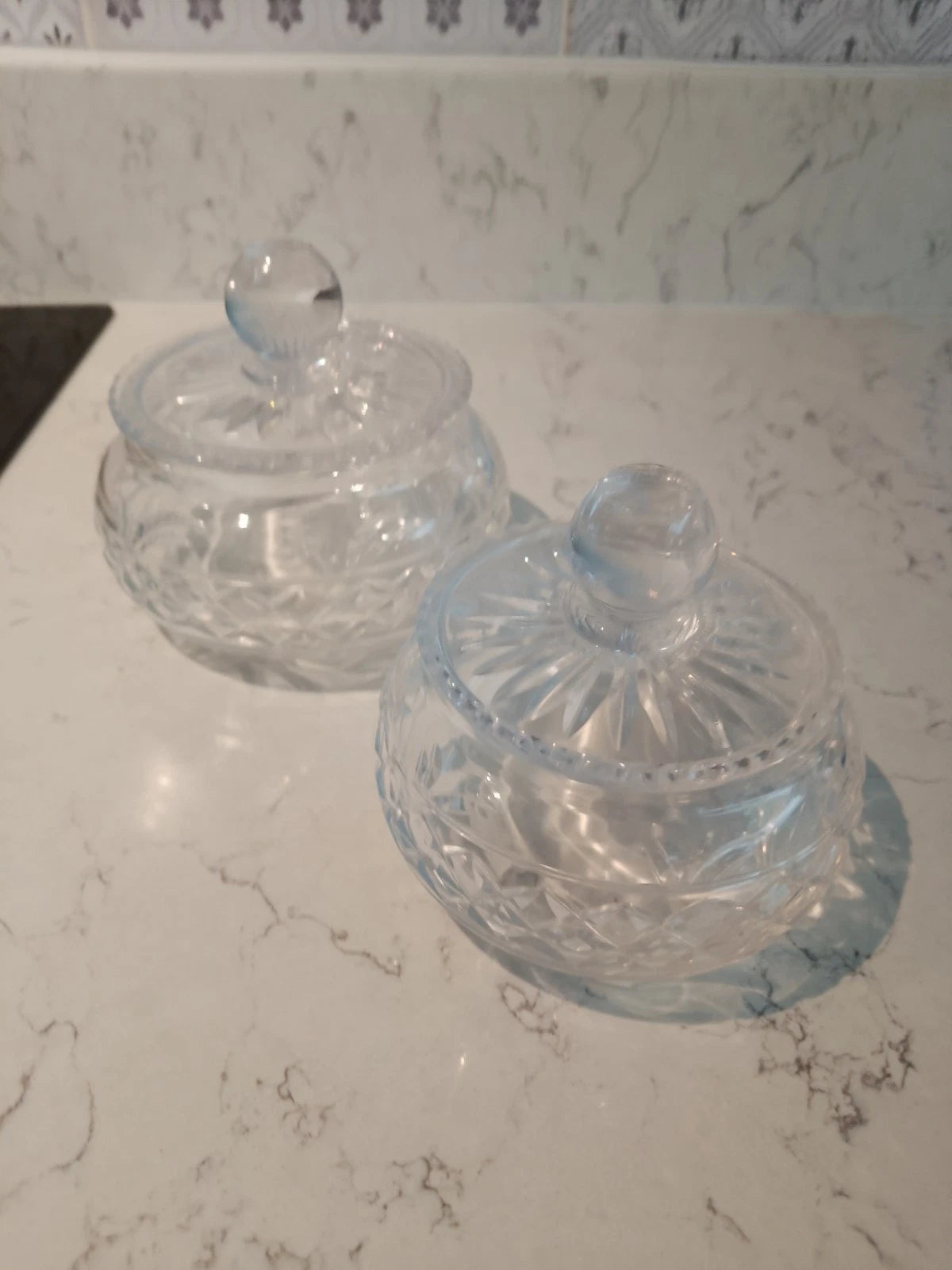 Pair of vintage Stuart crystal jars with intricate cut glass patterns and round lids on marble surface