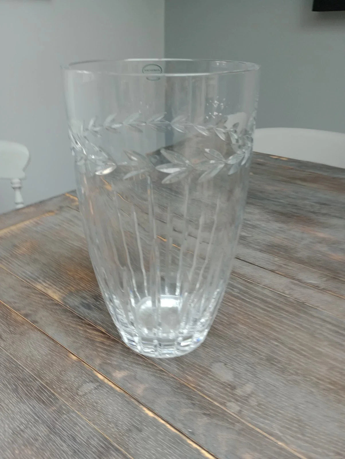 Clear collectible glassware vase with intricate leaf etching on wooden table in classic setting