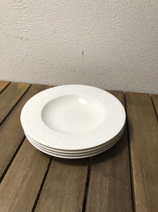 Stack of white Villeroy & Boch Cellini soup bowls with embossed pattern on wooden surface
