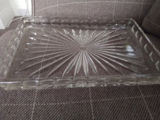 Clear vintage glass dressing table tray with intricate starburst pattern on brown fabric surface